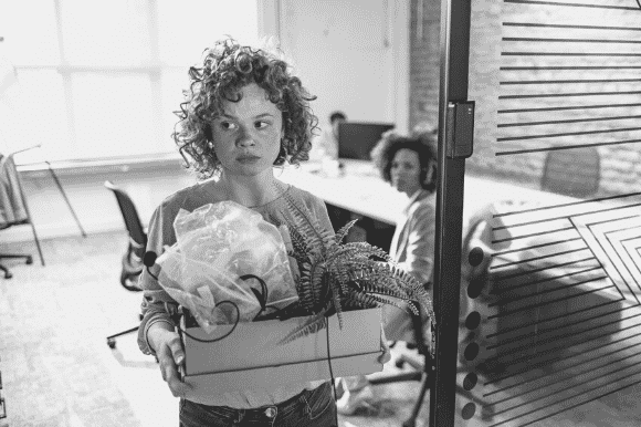 Unhappy worker with box of personal items after being terminated, illustrating employee turnover.