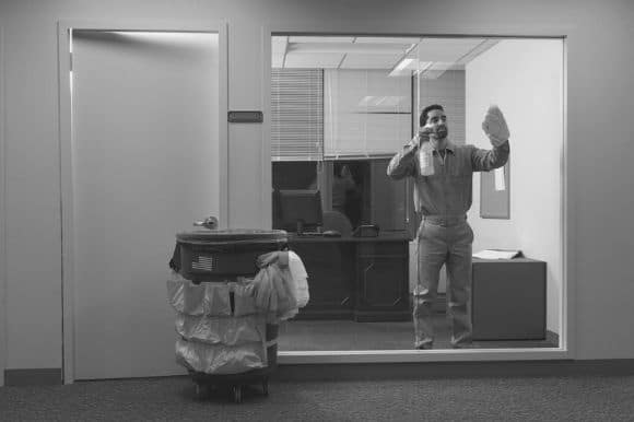 Cleaner wiping down a window and cleaning up an office.