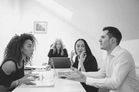 Four employees sitting around a conference room table, expressing heightened emotions in the workplace.